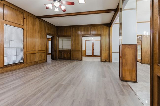 Unfurnished living room with light wood-style flooring, wood walls, beamed ceiling, and ceiling fan | Image 5