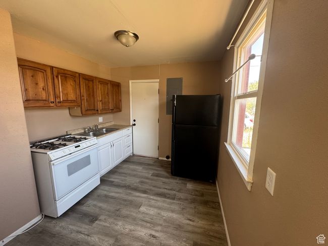 Kitchen featuring white gas range, freestanding refrigerator, brown cabinetry, dark wood finished floors, and electric panel | Image 6