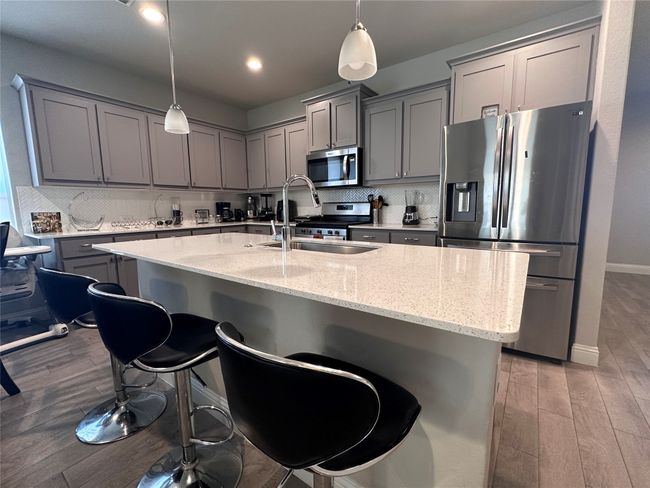 Kitchen with gray cabinets, stainless steel appliances, backsplash, light stone counters, and light wood finished floors | Image 6
