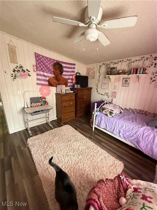 Bedroom with wooden walls, wood finished floors, a textured ceiling, and ceiling fan | Image 21