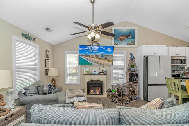 Living area with lofted ceiling, wood finished floors, a ceiling fan, and a lit fireplace | Image 5