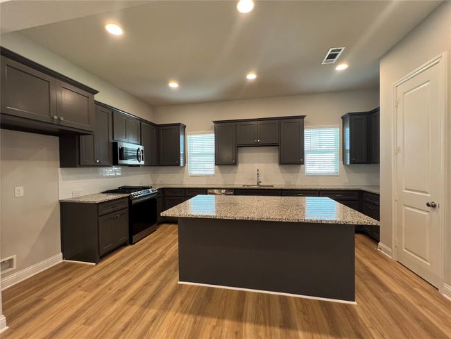 Kitchen featuring appliances with stainless steel finishes, a center island, a sink, tasteful backsplash, and light stone counters | Image 7
