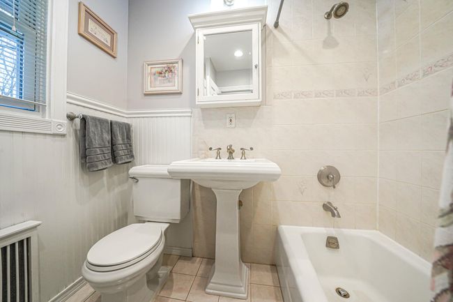 Full bathroom featuring bathtub / shower combination, toilet, radiator, wainscoting, and tile patterned flooring | Image 21