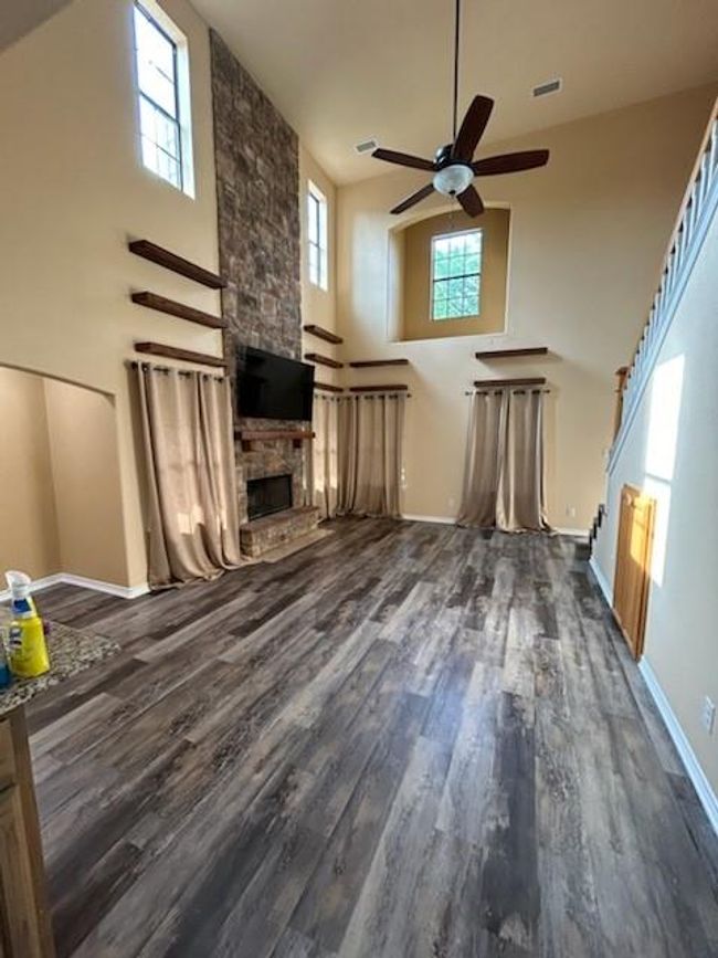 living room featuring dark hardwood / wood-style flooring, ceiling fan, a towering ceiling, and a fireplace | Image 8