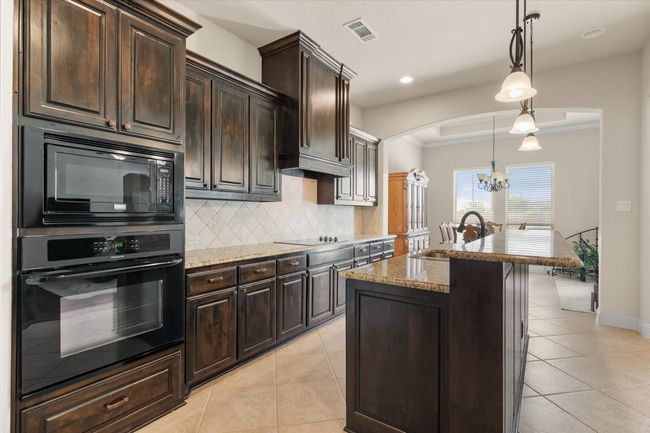 Kitchen with black appliances, a chandelier, light stone countertops, tasteful backsplash, and tile floors | Image 10
