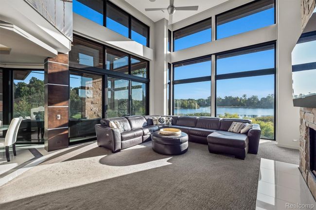Carpeted living room featuring a high ceiling, a stone fireplace, plenty of natural light, and a ceiling fan | Image 7