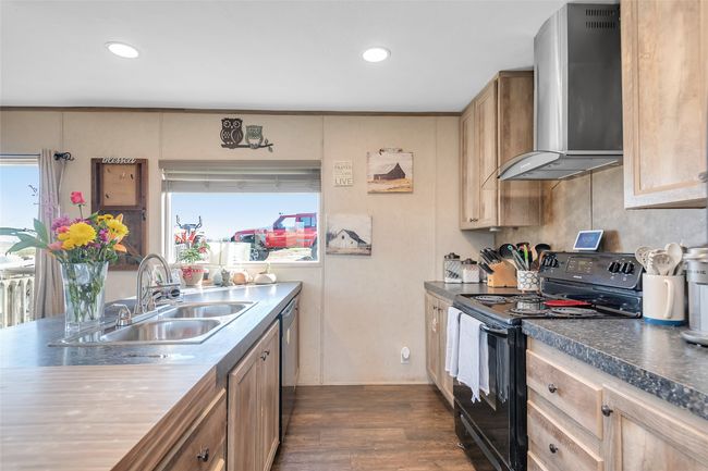 Kitchen with dishwashing machine, dark wood finished floors, a sink, black range with electric stovetop, and wall chimney exhaust hood | Image 20