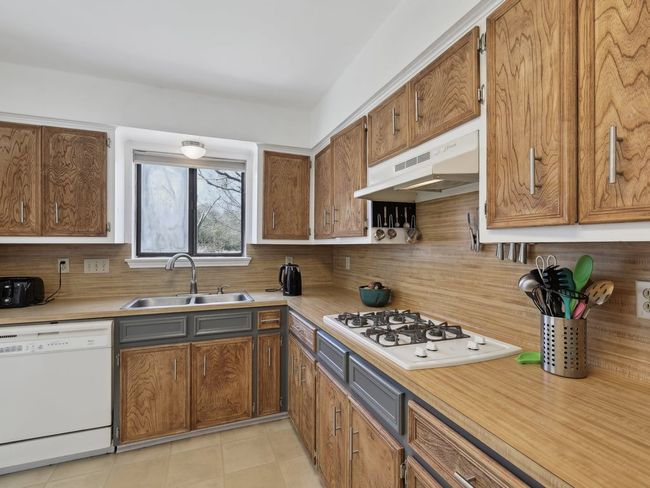 Kitchen with under cabinet range hood, white appliances, a sink, and backsplash | Image 10
