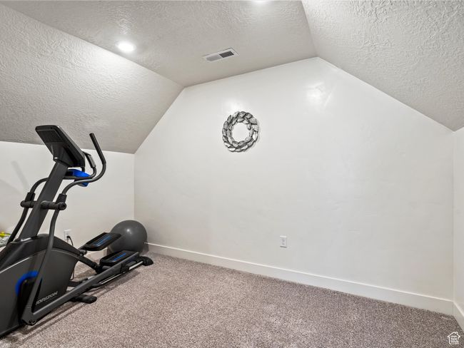 Exercise room with a textured ceiling, vaulted ceiling, carpet flooring, and baseboards | Image 25