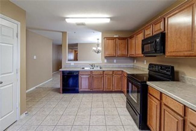 Kitchen featuring black appliances, brown cabinetry, light countertops, and light tile patterned floors | Image 4