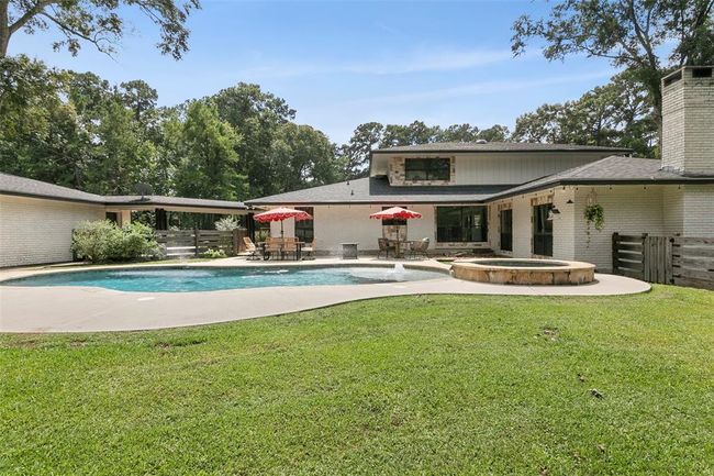 Spacious backyard featuring a large pool and hot tub, surrounded by a well-maintained lawn and mature trees. The modern home has a sleek exterior with large windows and a patio area ideal for outdoor entertaining. | Image 46