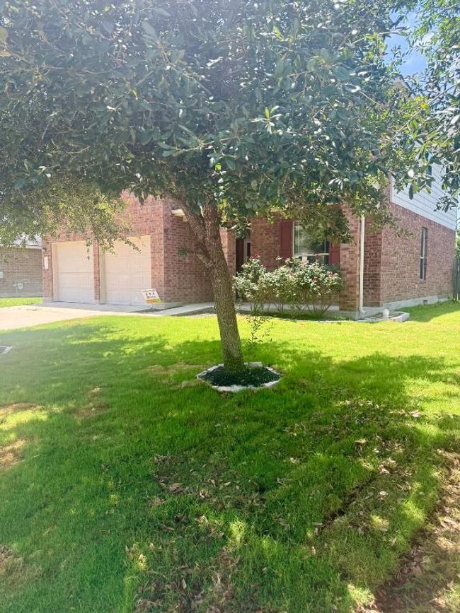 View of property hidden behind natural elements featuring brick siding, a front yard, driveway, and an attached garage | Image 4