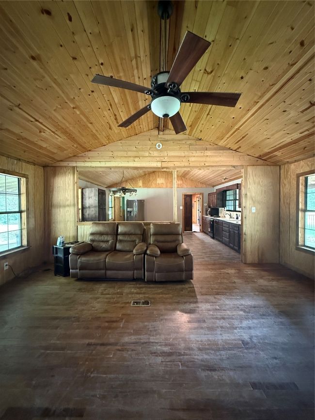 Living area featuring wood ceiling, dark wood-style flooring, lofted ceiling, a ceiling fan, and wood walls | Image 19
