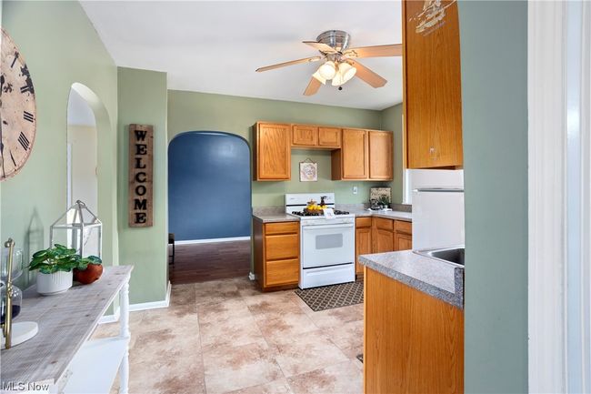 Kitchen featuring brown cabinets, light countertops, ceiling fan, light tile flooring, and white appliances | Image 8
