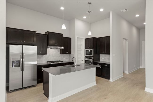 Kitchen featuring appliances with stainless steel finishes, tasteful backsplash, light wood finished floors, a towering ceiling, and hanging light fixtures | Image 17