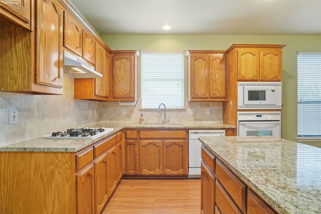 Kitchen featuring decorative backsplash, light wood finished floors, white appliances, under cabinet range hood, and a sink | Image 9