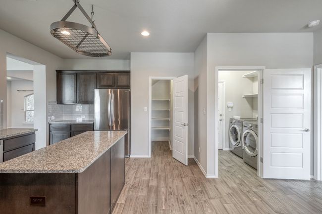Kitchen featuring washing machine and clothes dryer, freestanding refrigerator, light wood finished floors, dark brown cabinetry, and recessed lighting | Image 9