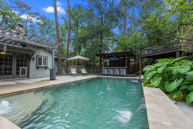 This photo showcases a serene backyard with a sparkling pool, surrounded by lush greenery. There's a stylish pergola-covered patio, perfect for outdoor relaxation, and a poolside bar area that adds an entertaining touch- Ideal for enjoying nature and hosting gatherings! | Image 37