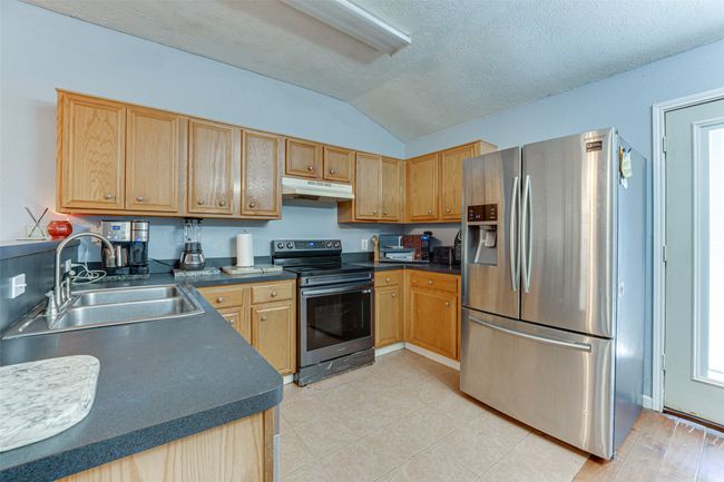 Kitchen with lofted ceiling, under cabinet range hood, stainless steel appliances, dark countertops, and a sink | Image 18