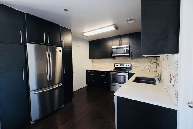 Kitchen featuring dark cabinets, stainless steel appliances, tasteful backsplash, and dark wood-type flooring | Image 16