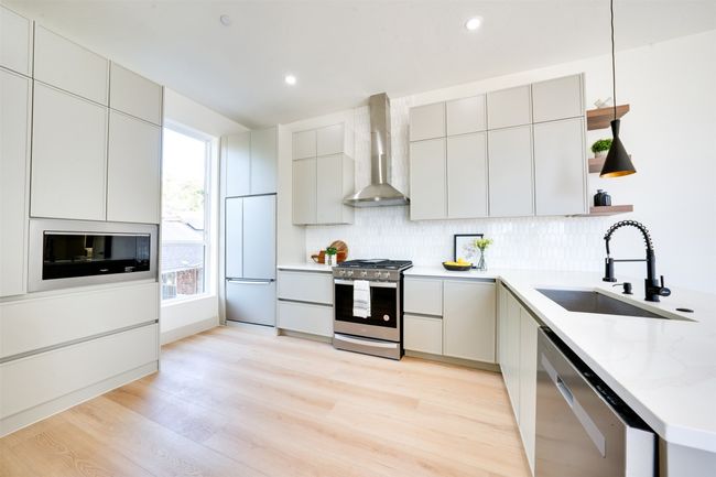 Kitchen with wall chimney exhaust hood, hanging light fixtures, stainless steel appliances, sink, and light hardwood / wood-style floors | Image 14