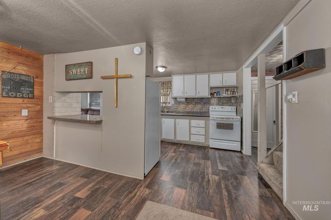 Kitchen featuring electric stove, freestanding refrigerator, wood walls, dark countertops, and dark wood finished floors | Image 9