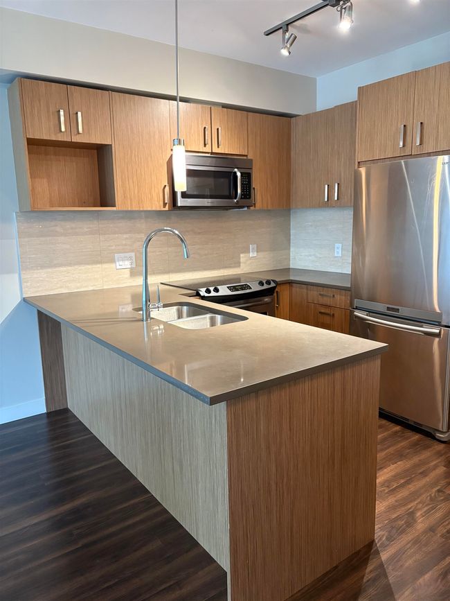 Kitchen with decorative backsplash, appliances with stainless steel finishes, a sink, a peninsula, and dark wood-type flooring | Image 6
