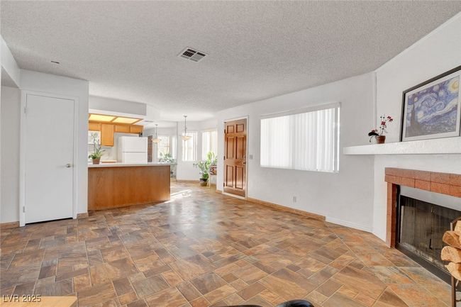 Unfurnished living room featuring a tiled fireplace, visible vents, a textured ceiling, and baseboards | Image 4
