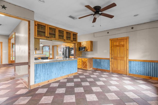 Kitchen with glass insert cabinets, a ceiling fan, black appliances, visible vents, and a wainscoted wall | Image 14
