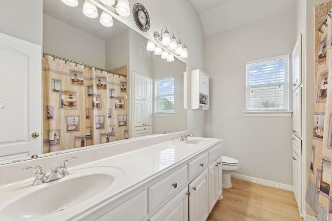Bathroom with toilet, double vanity, baseboards, wood finished floors, and vaulted ceiling | Image 25