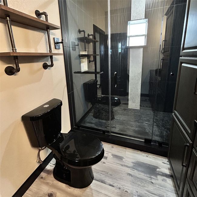 Modern bathroom featuring a sleek black toilet, industrial-style shelving, and a spacious glass-enclosed shower with dark tiles. | Image 15