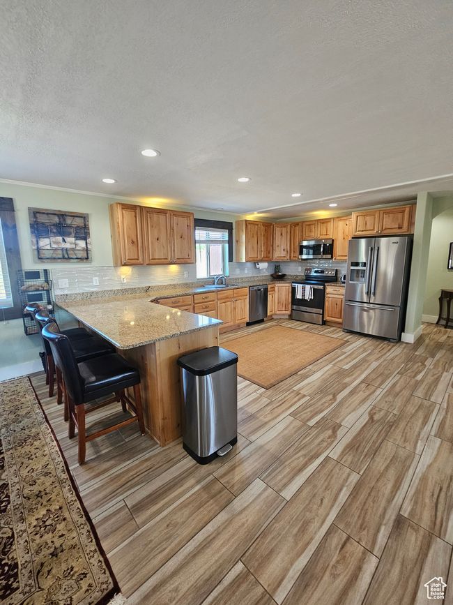 Kitchen featuring stainless steel appliances, granite countertops, a bar, decorative backsplash, knotty alder cabinets and beautiful flooring | Image 33