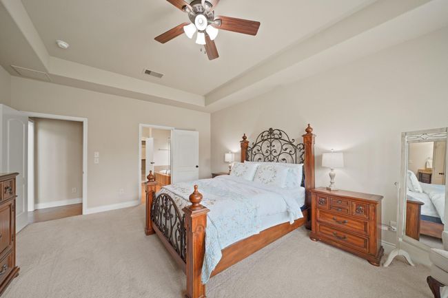 This cozy bedroom features soft carpeting, neutral walls, and a ceiling fan for comfort. There's plenty of natural light and a spacious feel. | Image 20