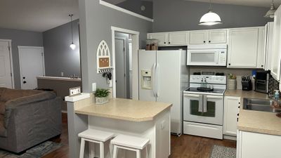 Kitchen with dark wood-type flooring, white cabinets, pendant lighting, and white appliances | Image 2