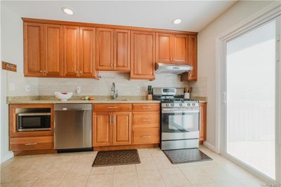 Kitchen featuring light tile patterned floors, light stone counters, sink, decorative backsplash, and appliances with stainless steel finishes | Image 2