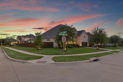 This photo features a spacious corner lot home in a serene suburban setting, showcasing well-manicured lawns and a picturesque sunset sky. The neighborhood appears peaceful and well-maintained, with attractive single-family homes lining the street. | Image 2