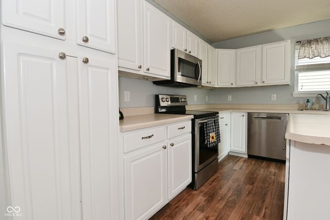 kitchen with appliances with stainless steel finishes, dark wood-type flooring, white cabinetry, light countertops, and a sink | Image 19