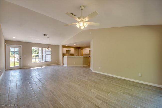 Unfurnished living room with ceiling fan with notable chandelier, visible vents, baseboards, vaulted ceiling, and light wood finished floors | Image 20