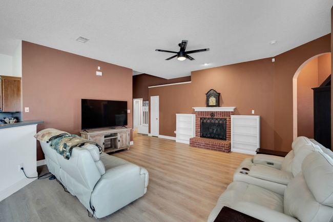 Living area with arched walkways, a ceiling fan, light wood finished floors, and a fireplace | Image 9