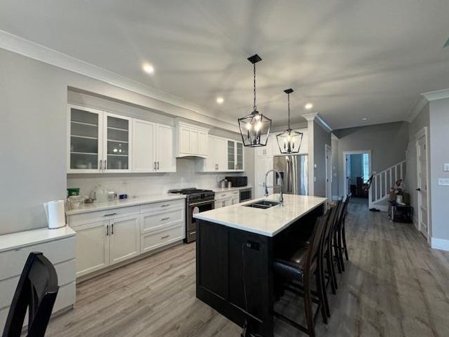 Kitchen with a sink, light wood-type flooring, white cabinetry, appliances with stainless steel finishes, and ornamental molding | Image 23