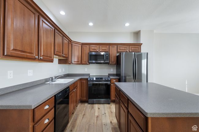 Kitchen with appliances with stainless steel finishes, light wood-type flooring, recessed lighting, brown cabinets, and dark countertops | Image 5