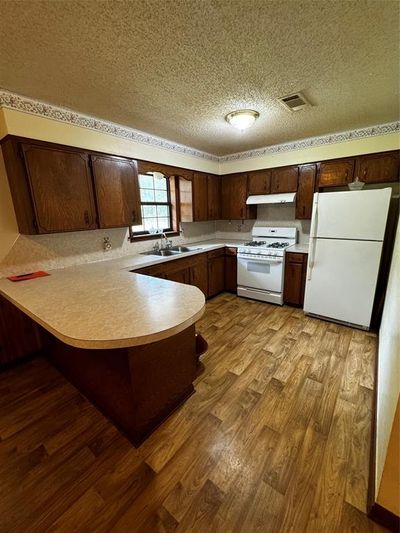 Kitchen with light wood-type flooring, fridge, kitchen peninsula, range, and a textured ceiling | Image 3