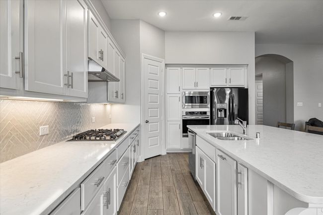 Kitchen with arched walkways, wood finished floors, a sink, under cabinet range hood, and stainless steel appliances | Image 6