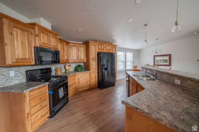 Kitchen with hanging light fixtures, a sink, black appliances, light wood-style flooring, and backsplash | Image 25