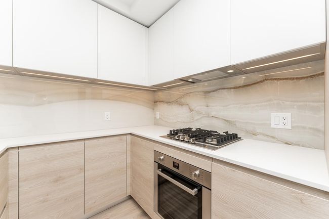 Kitchen with modern cabinets, light brown cabinetry, light countertops, stainless steel appliances, and decorative backsplash | Image 9