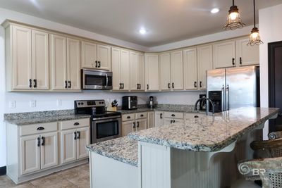 Kitchen with light stone countertops, a kitchen island, appliances with stainless steel finishes, decorative light fixtures, and a breakfast bar | Image 2