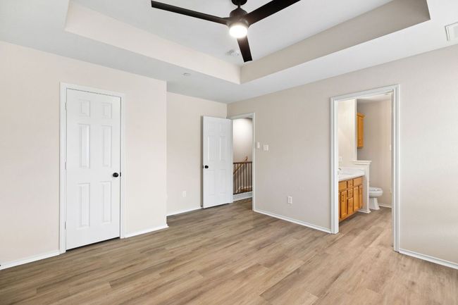 Unfurnished bedroom featuring light wood-style flooring, a tray ceiling, visible vents, baseboards, and ensuite bath | Image 18