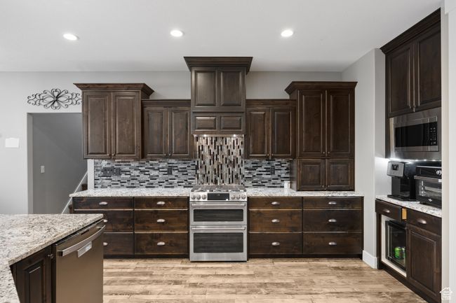 Kitchen featuring appliances with stainless steel finishes, decorative backsplash, dark brown cabinetry, light wood-style flooring, vented hood, and recessed lighting | Image 9