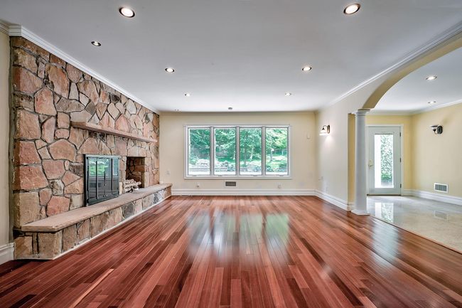 Unfurnished living room featuring arched walkways, a stone fireplace, visible vents, plenty of natural light, and ornate columns | Image 6