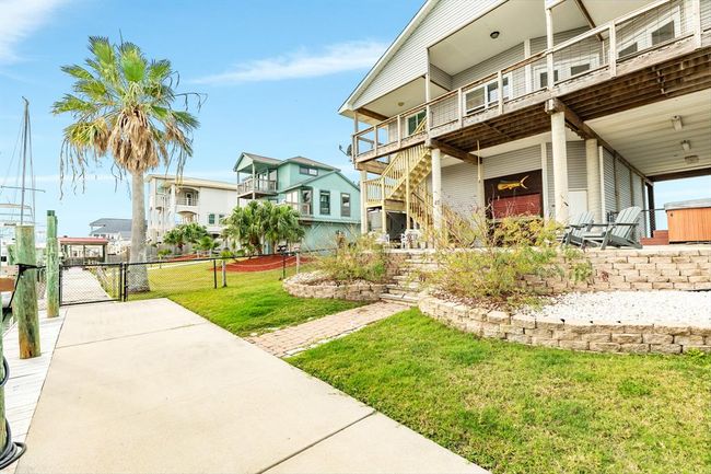 This canal front property features an elevated, modern home with spacious decking, a hot tub, and a well-maintained yard. It offers easy access to the water, surrounded by lush greenery and neighboring homes, creating a serene coastal living environment. | Image 26